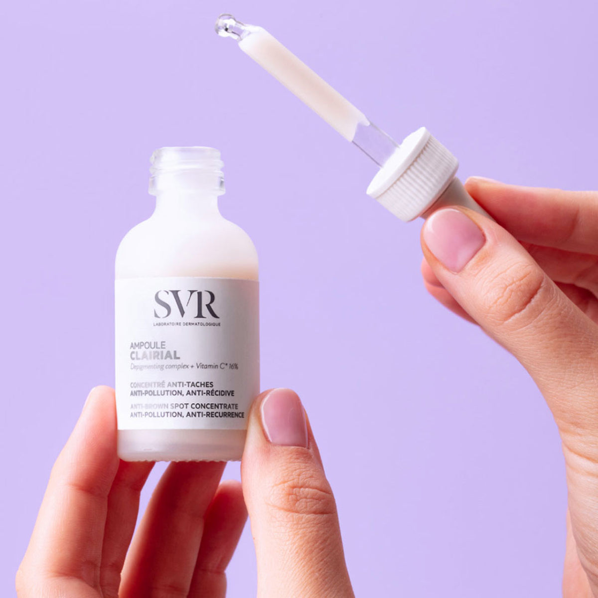 Flacon en verre dépoli SVR Clairial Ampoule avec pipette compte-gouttes tenue par des mains sur fond violet.