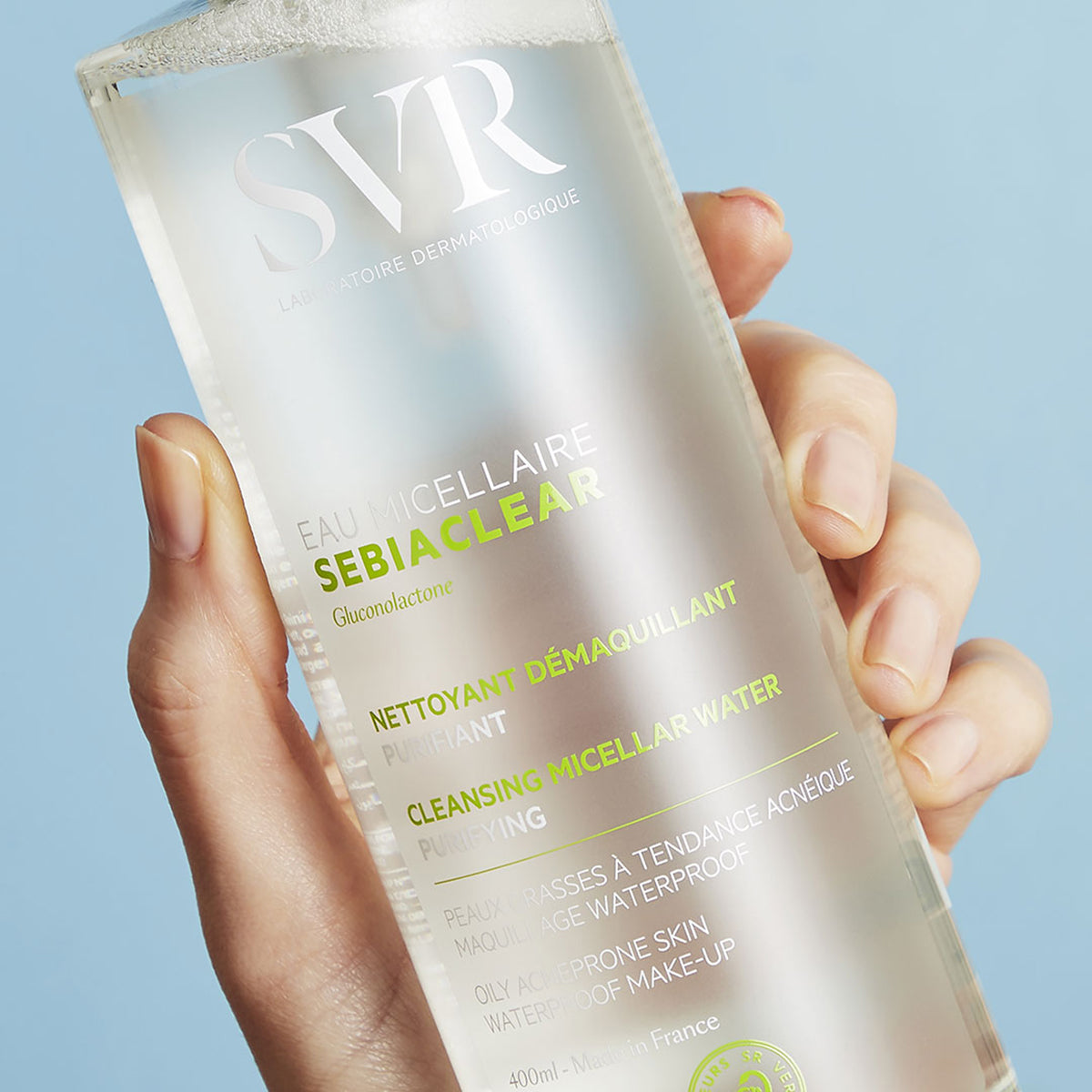 Flacon transparent de 400ml d'eau micellaire SVR Sebiaclear tenu en main, nettoyant purifiant pour peaux à tendance acnéique.