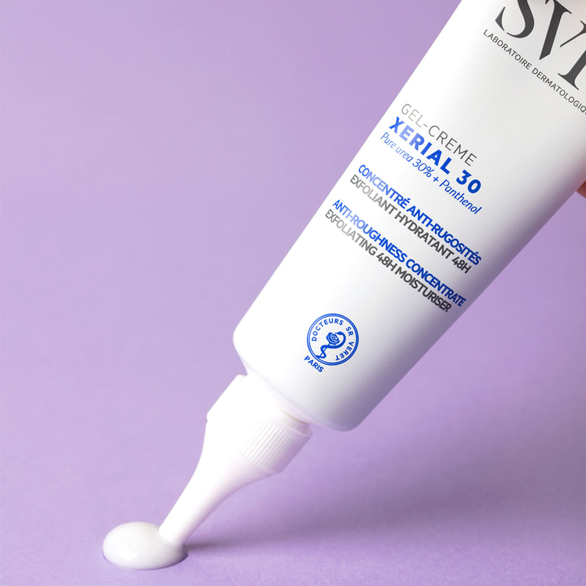 Tube blanc de gel-crème SVR Xerial 30 distribuant une noisette de produit sur un fond violet uni.