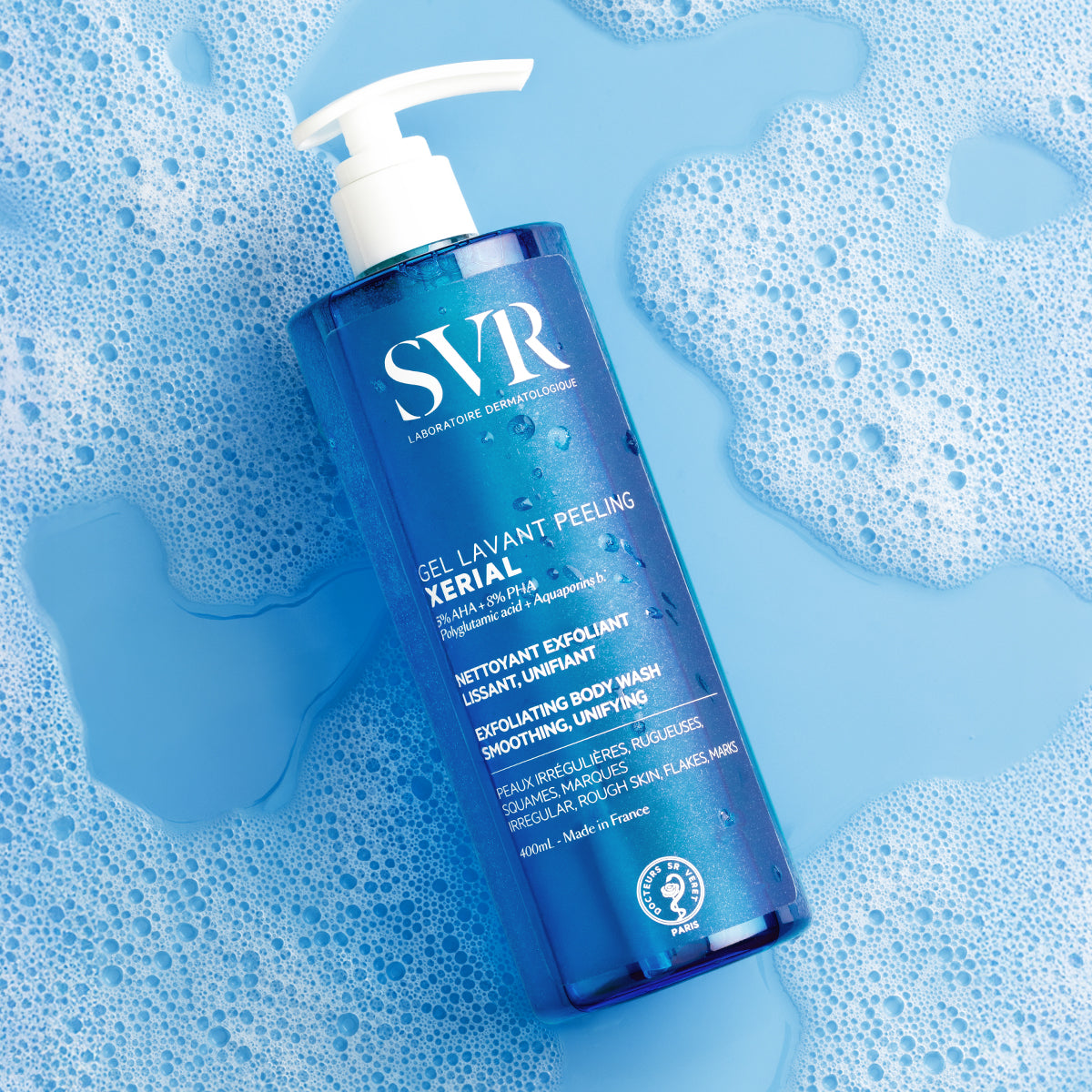 SVR XERIAL Gel Lavant Peeling 400ml bottle with white pump, resting on a blue soapy water background with foam bubbles.