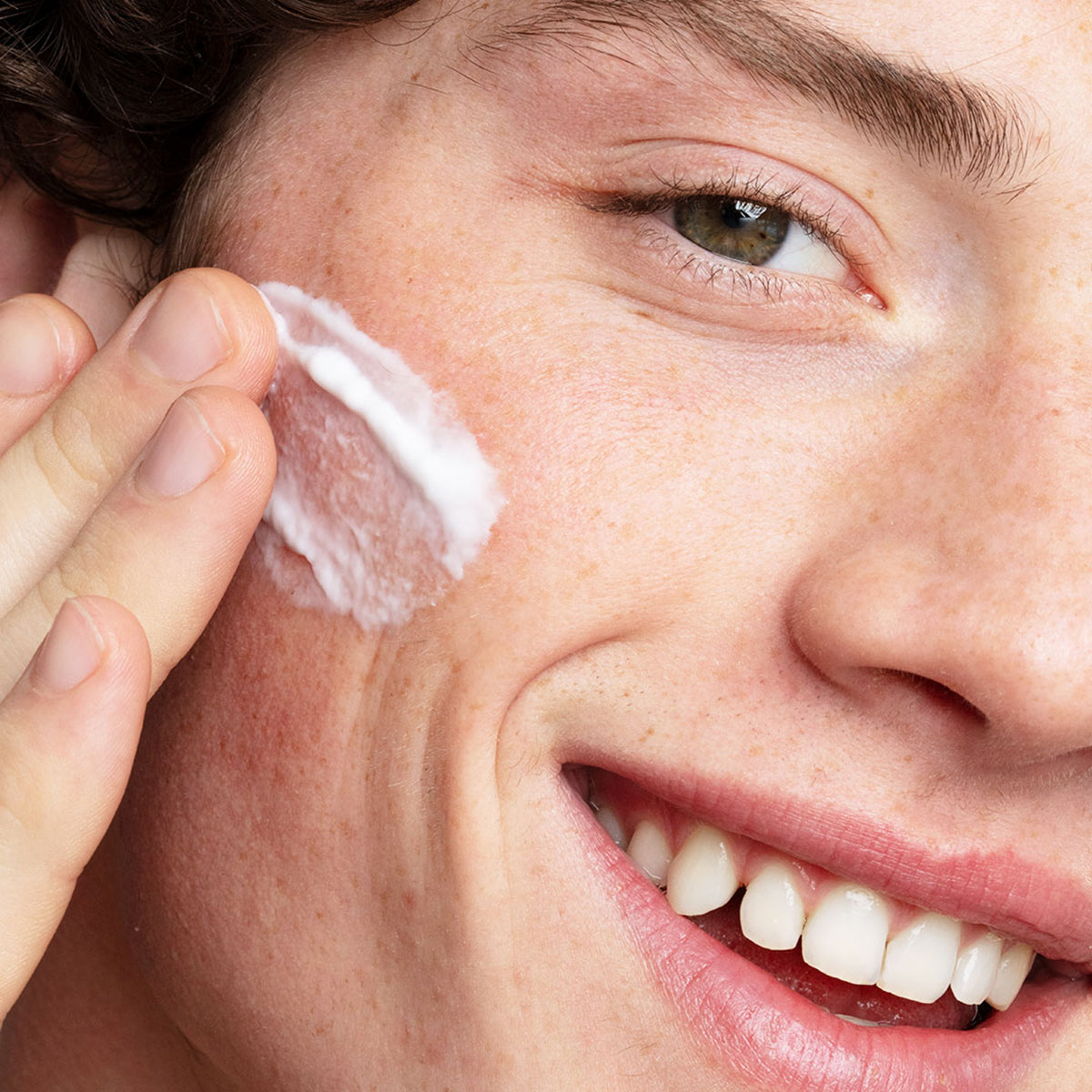 Personne souriante appliquant une texture crème blanche légère et hydratante sur sa joue pour le soin Hydraliane.