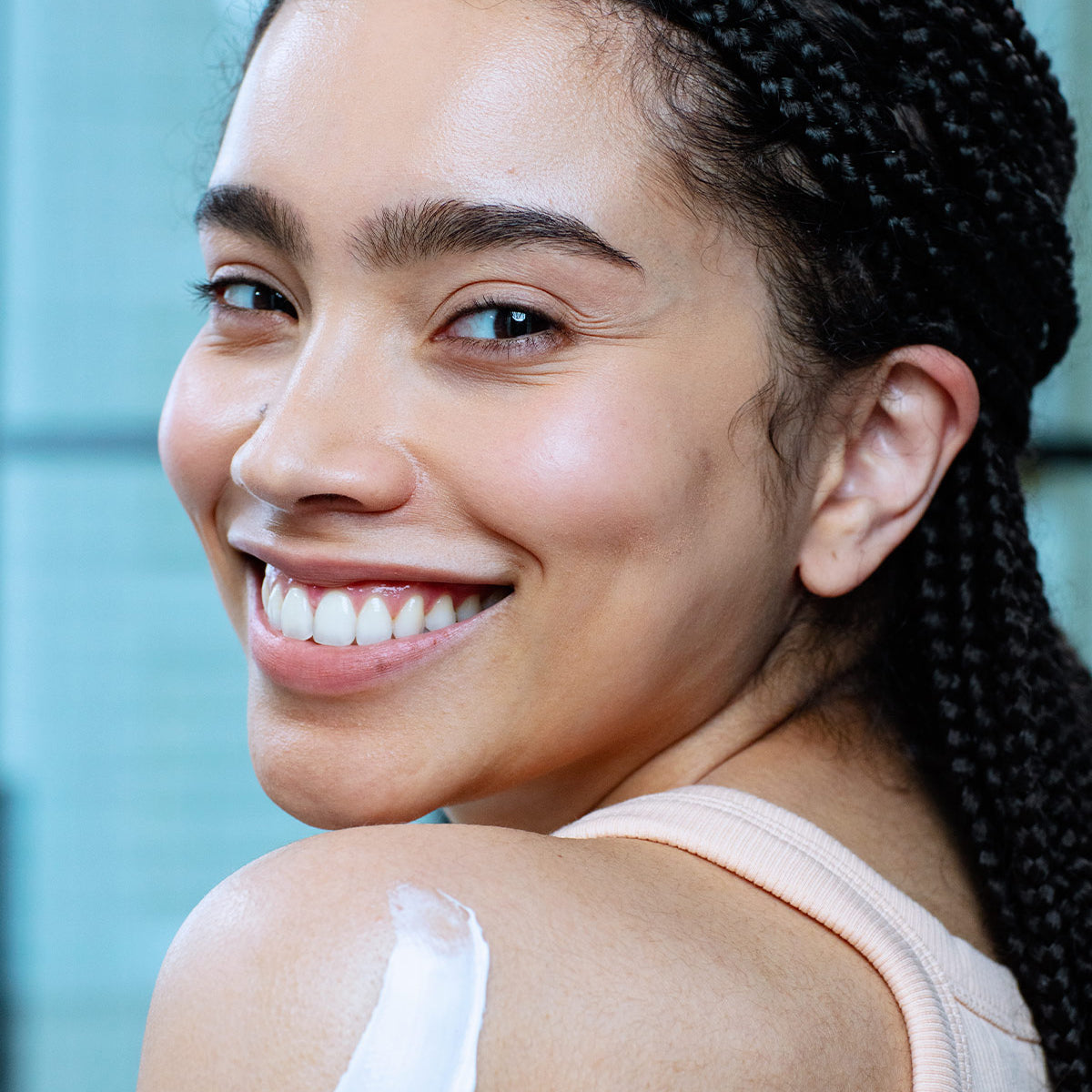 Jeune femme souriante appliquant une noisette de lait hydratant XERIAL 10 sur son épaule pour une peau douce et lisse.