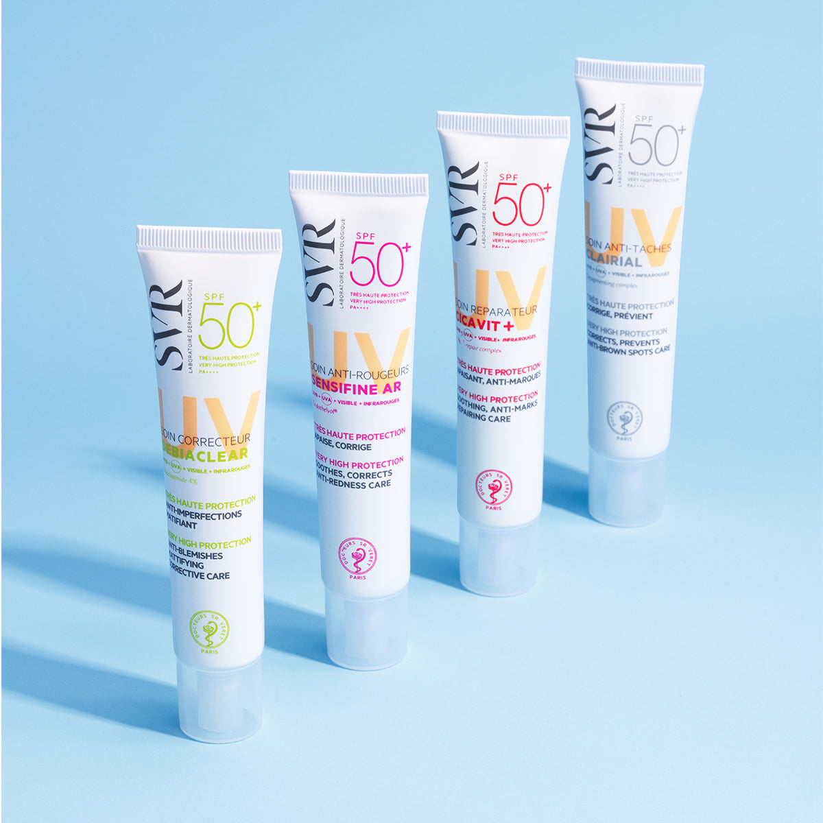 Quatre tubes blancs de crème solaire SVR SPF50+ alignés sur un fond bleu clair, mettant en avant les gammes Sebiaclear et Cicavit.