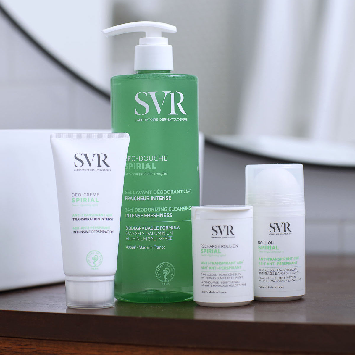 Gamme SVR Spirial : tube de crème anti-transpirante, flacon pompe de gel douche vert et deux déodorants roll-on sur un meuble.