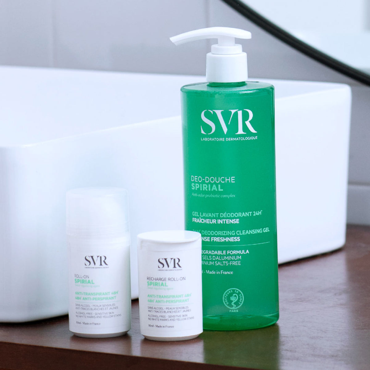 SVR Spirial roll-on, recharge, and green Deo-Douche cleansing gel bottles arranged on a bathroom counter.