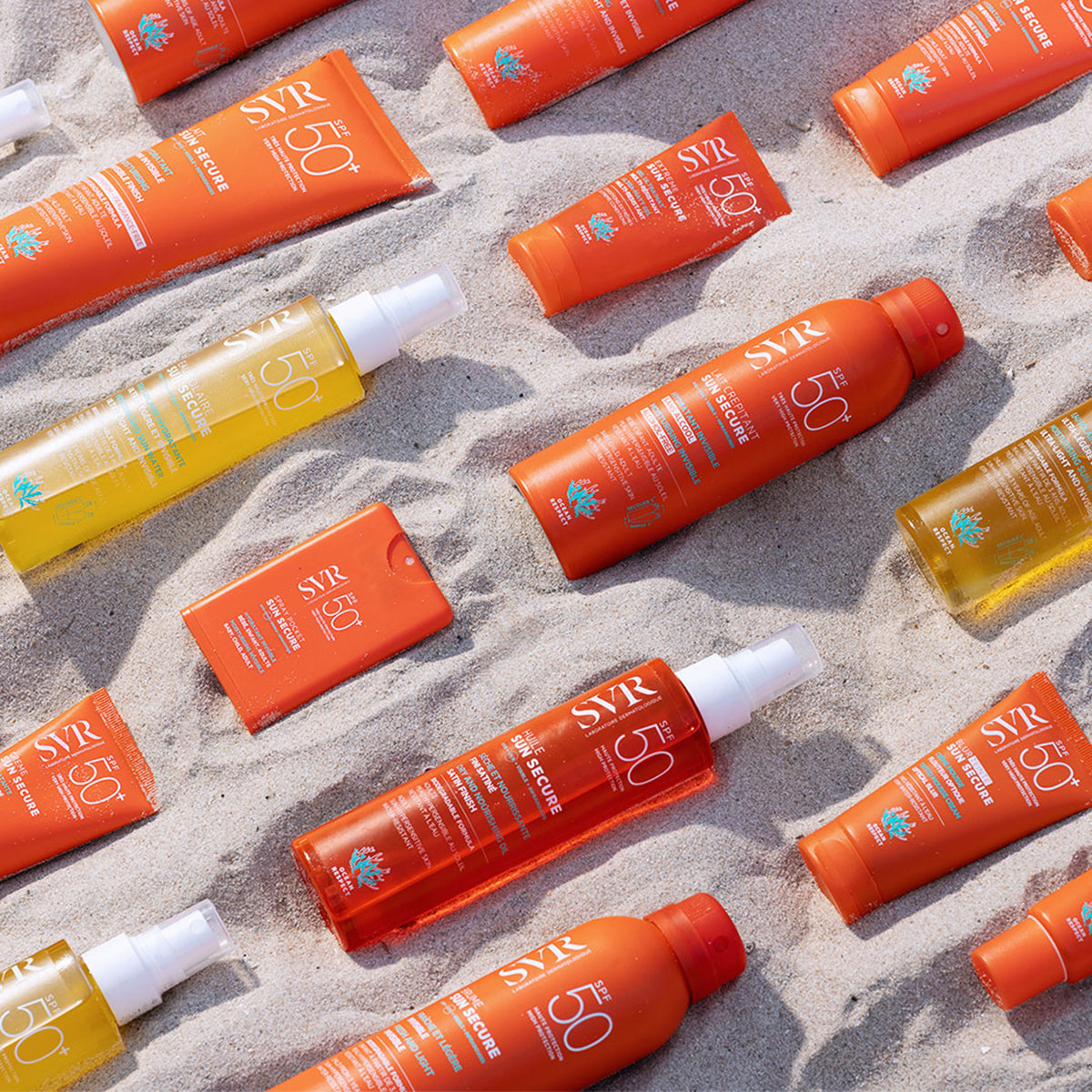 Assortiment de produits solaires SVR Sun Secure SPF50+ en tubes et flacons orange vif disposés sur le sable d'une plage.