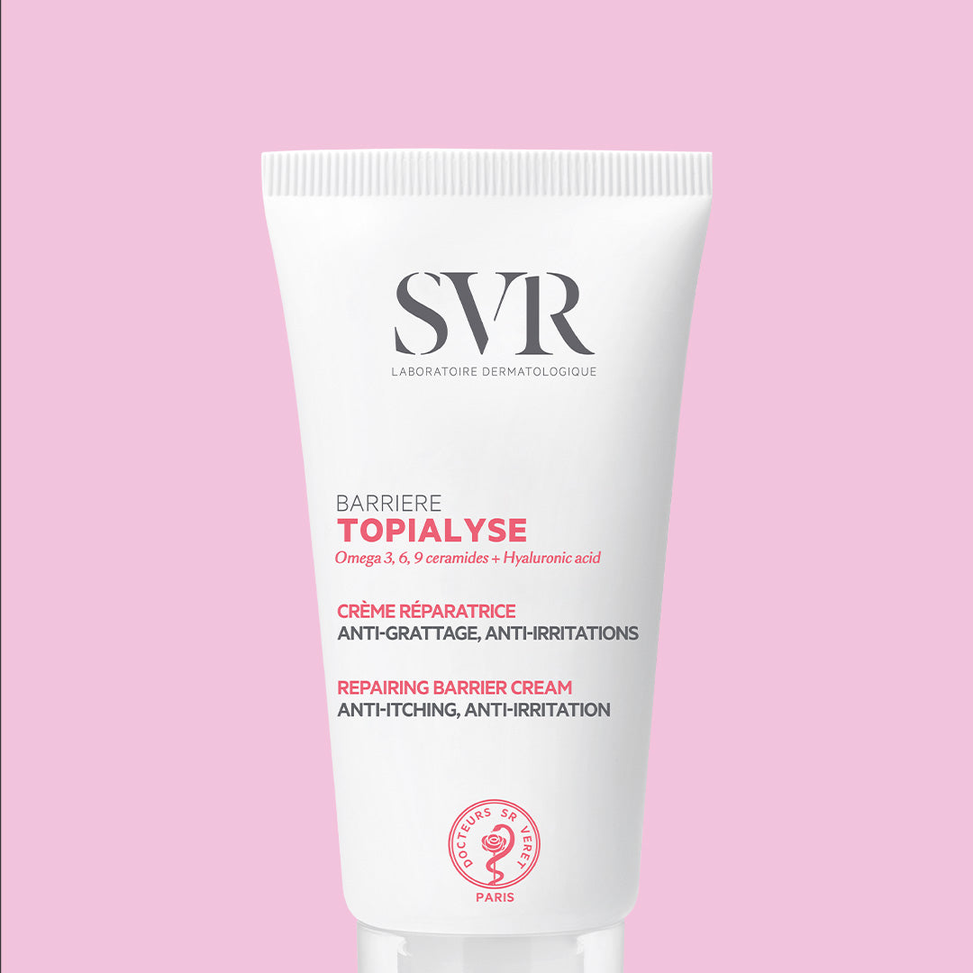 Tube blanc de crème réparatrice SVR Topialyse Barrière avec texte rose et noir sur fond rose pastel.