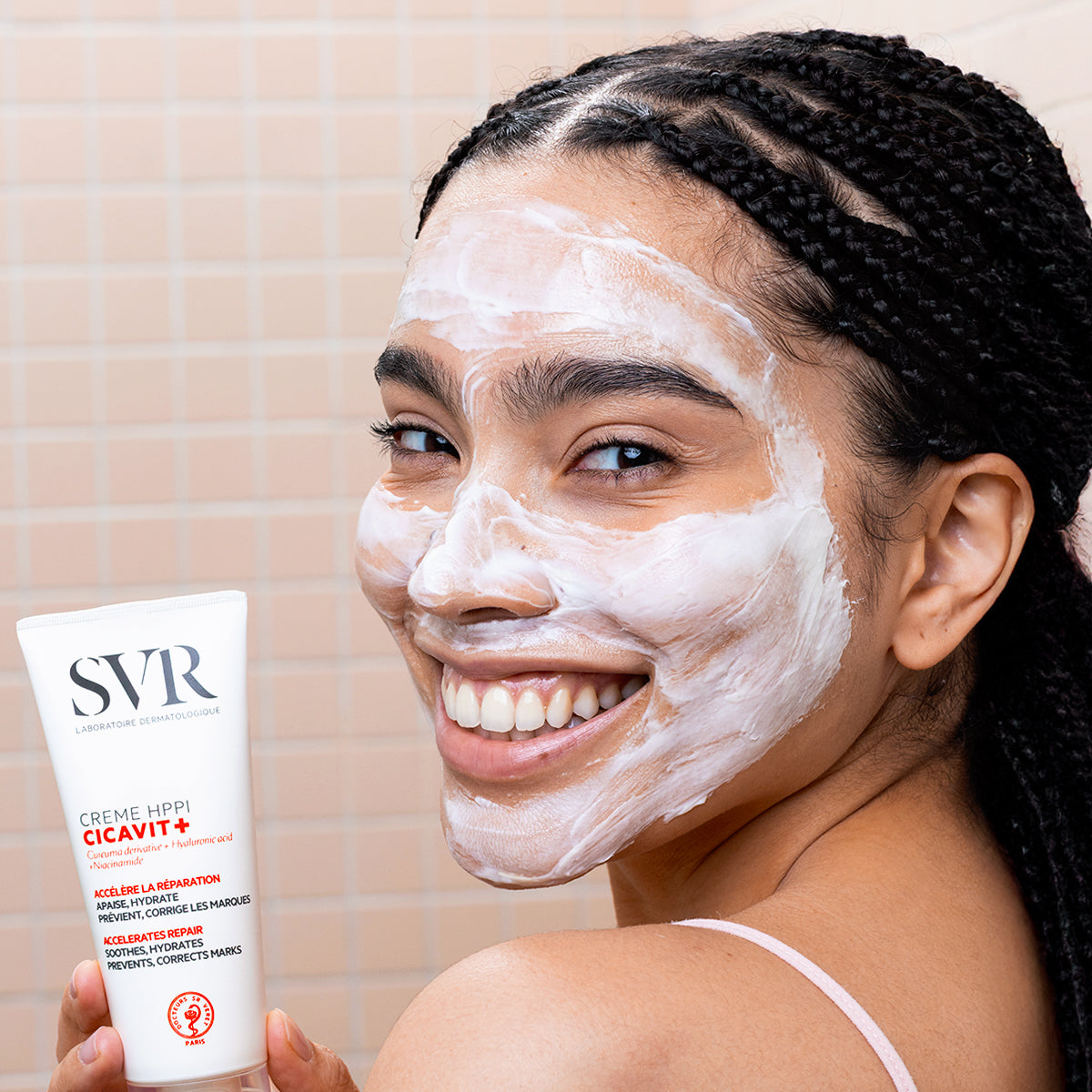 Smiling woman with white CICAVIT+ HPPI Crème on her face holding the white SVR skincare tube.