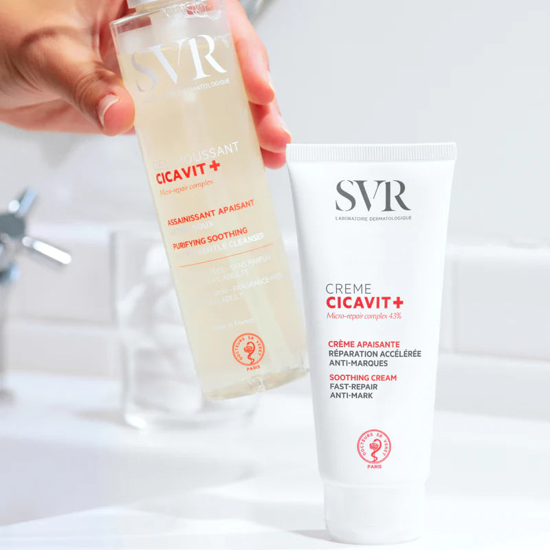 Flacon de gel moussant et tube de crème réparatrice SVR Cicavit+ blancs sur fond de salle de bain lumineuse.