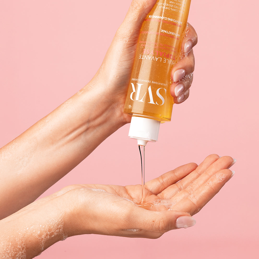 SVR TOPIALYSE Huile Lavante cleansing oil pouring from a clear bottle into a hand against a soft pink background.