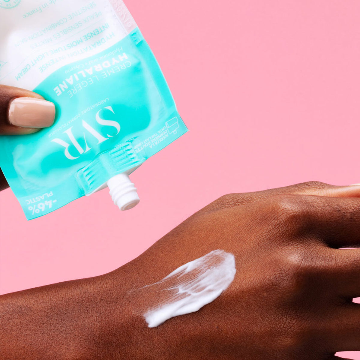 Poche éco-conçue SVR Hydraliane Crème Légère turquoise appliquée sur une main, texture blanche hydratante sur fond rose.
