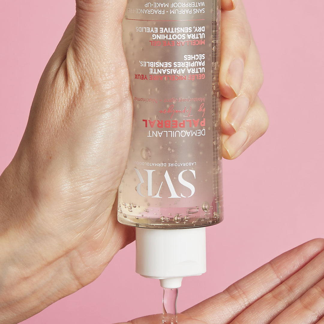 Main tenue à l'envers versant le gel démaquillant transparent SVR Palpebral sur une paume sur fond rose.