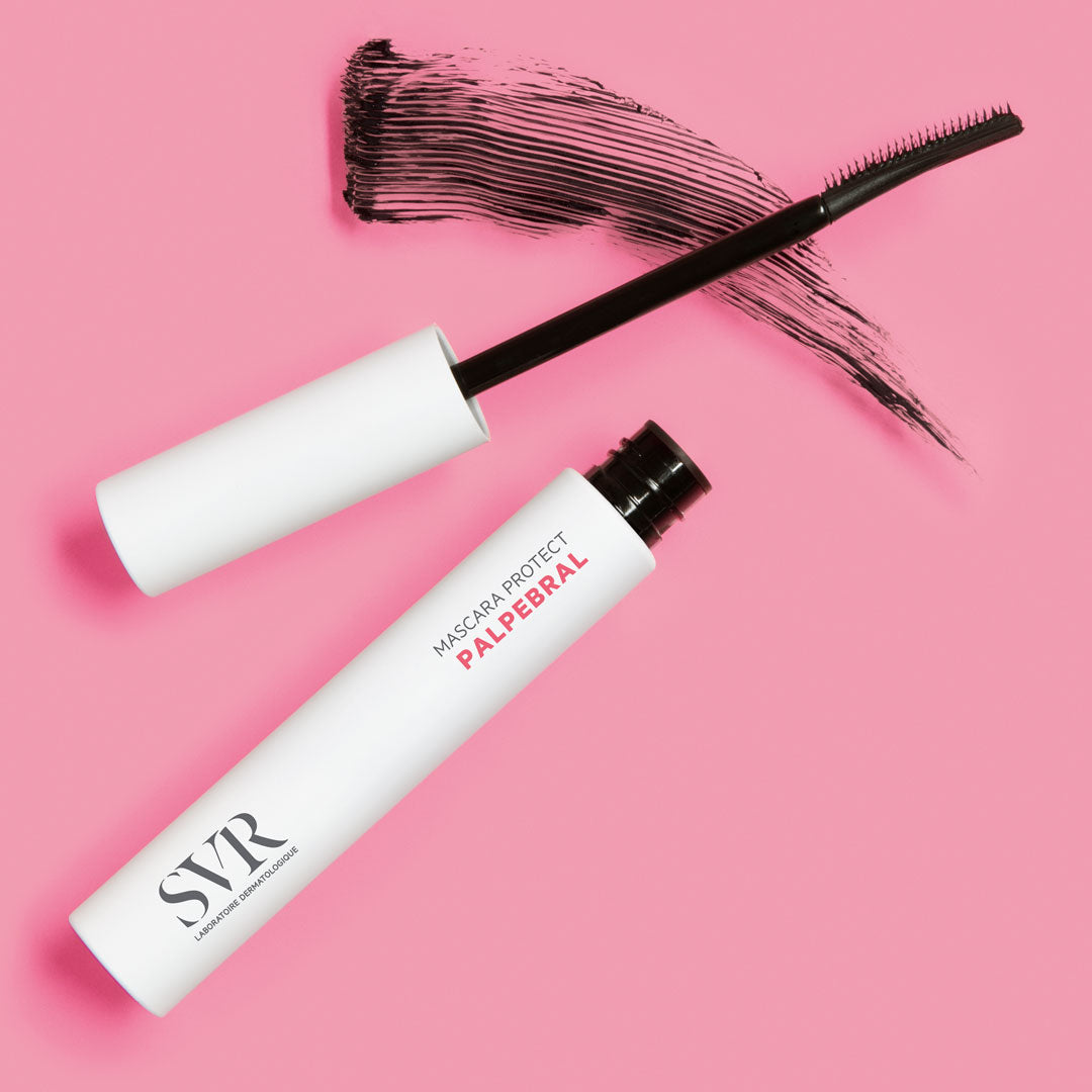 Tube de mascara blanc SVR Palpebral Protect avec applicateur et trace de mascara noir sur fond rose.