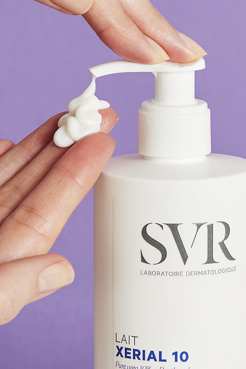 Flacon blanc SVR XERIAL 10 Lait avec pompe, texture crème onctueuse déposée sur une main, fond violet.