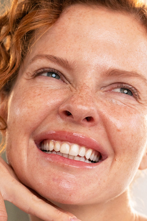 Close-up of a smiling woman with red hair and freckles, showcasing radiant, healthy skin for DENSITIUM Bi-Sérum.
