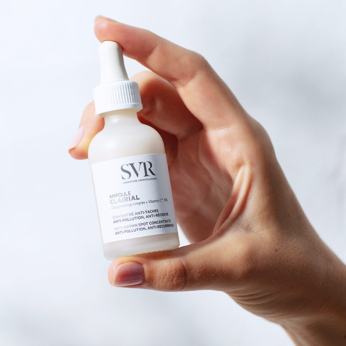 Main tenue par une main, flacon compte-gouttes en verre dépoli SVR Clairial Ampoule anti-taches avec étiquette blanche.