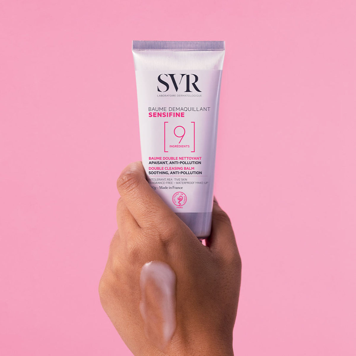 Main tenue en main présentant le tube de baume démaquillant SVR Sensifine avec une noisette de texture sur la peau.
