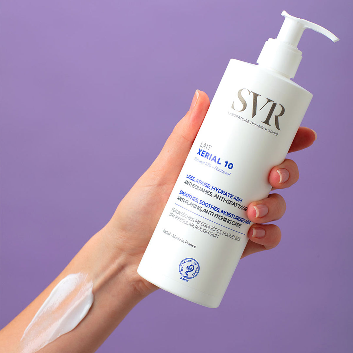 Flacon pompe blanc de lait hydratant SVR Xerial 10 de 400ml tenu en main avec une texture crémeuse appliquée sur le bras.