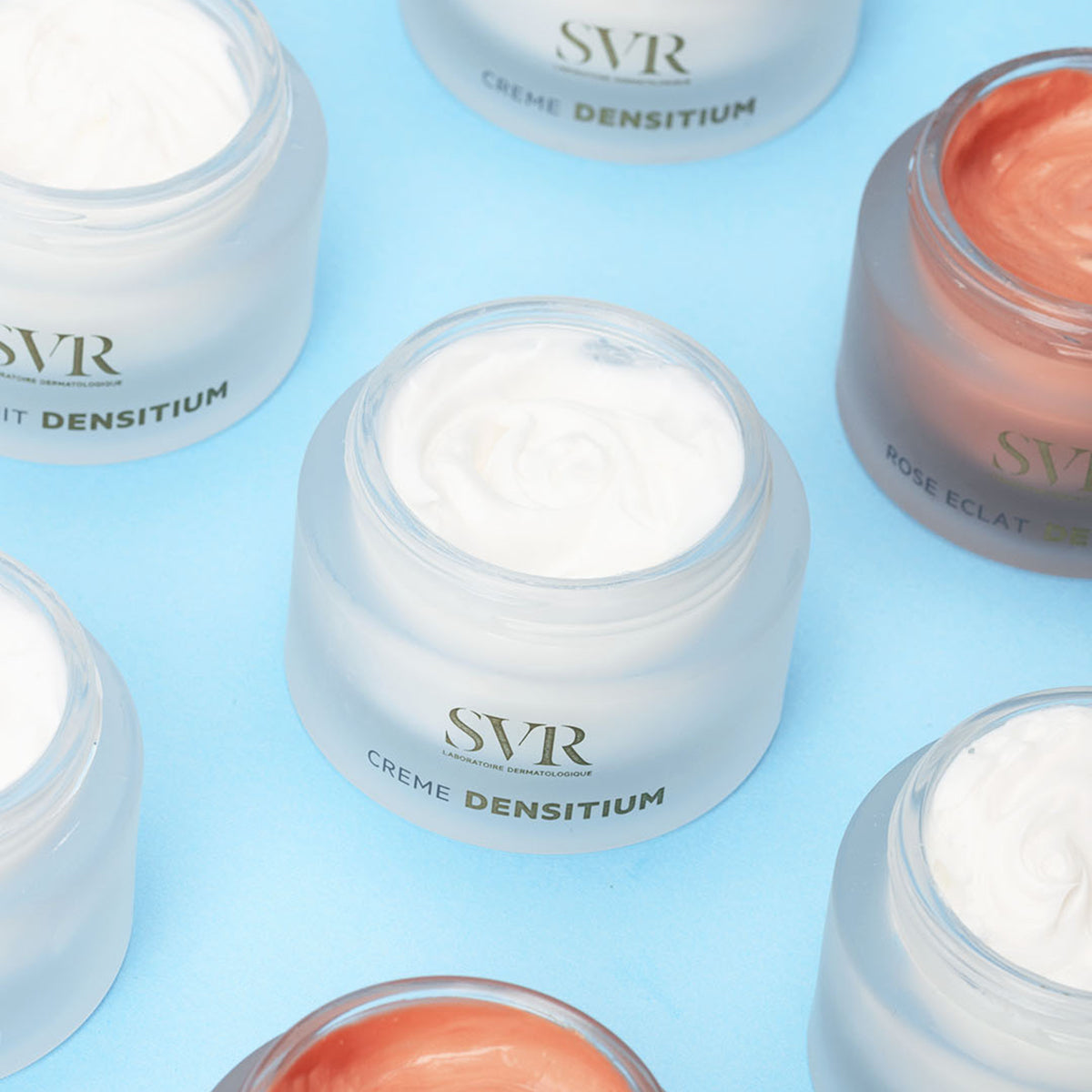 Open jars of SVR Densitium Crème riche with white and rose-tinted face cream on a light blue background.