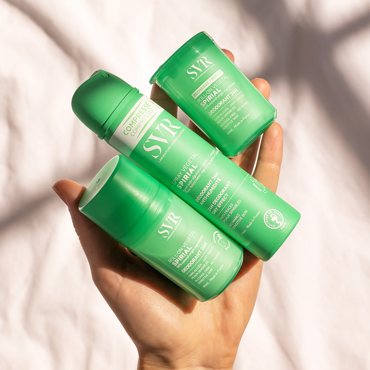 Main tenue en main présentant trois déodorants SVR Spirial Végétal verts : un roll-on, une recharge et un spray compressé.