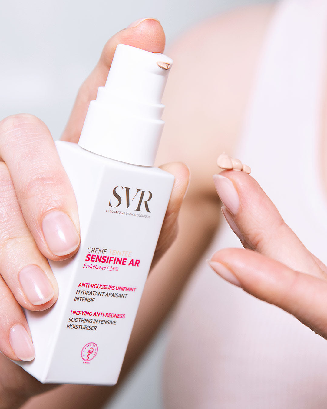 Flacon pompe blanc SVR Sensifine AR Crème Teintée avec une noisette de crème beige sur le doigt pour peaux couperosiques.