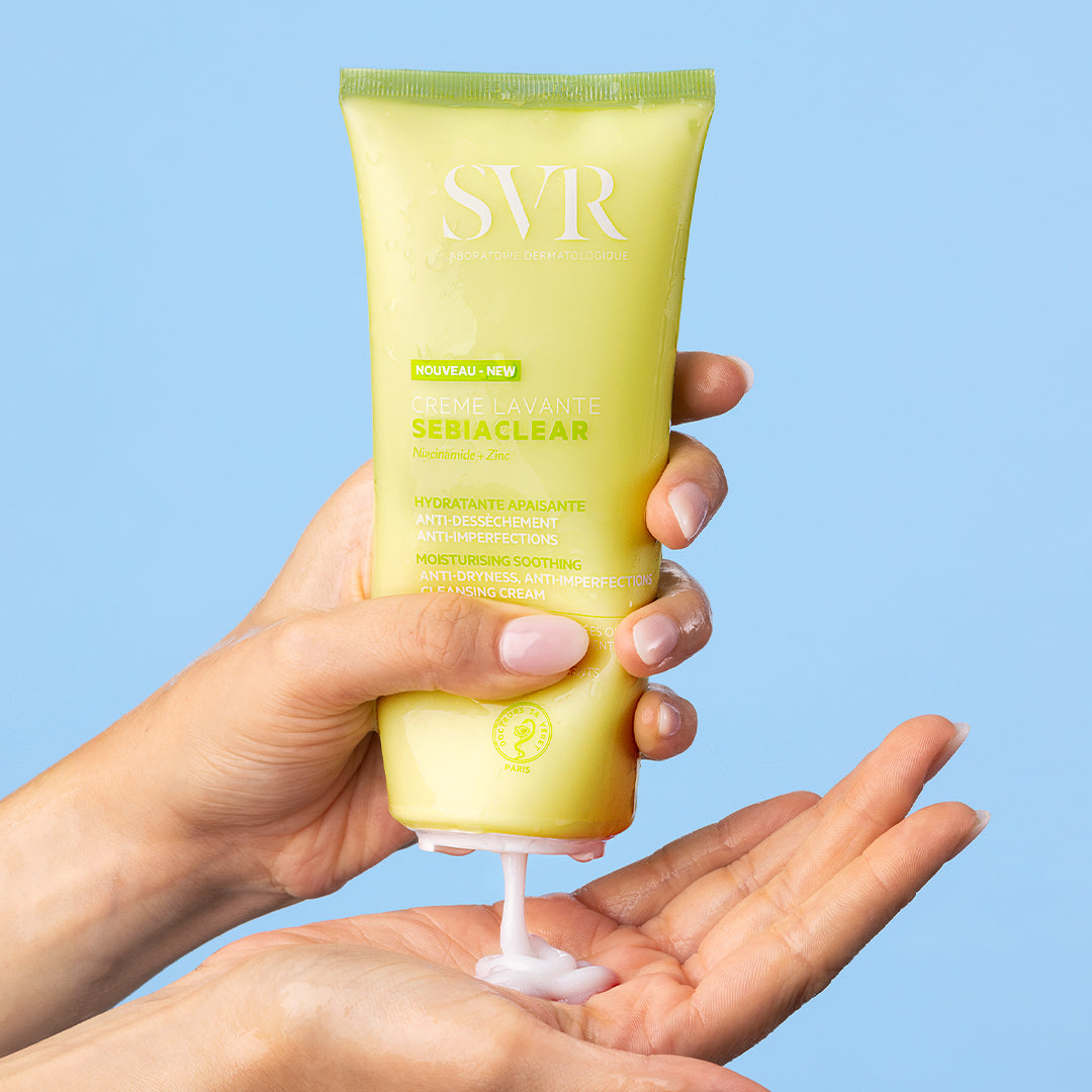 Tube jaune de crème lavante SVR Sebiaclear pressé dans une main, délivrant une texture onctueuse sur fond bleu clair.