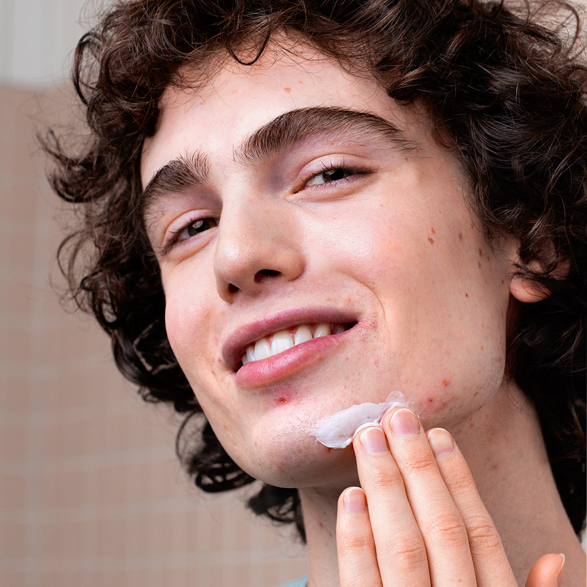 Young man with curly hair applying white CICAVIT+ HPPI Crème to a blemish on his chin.