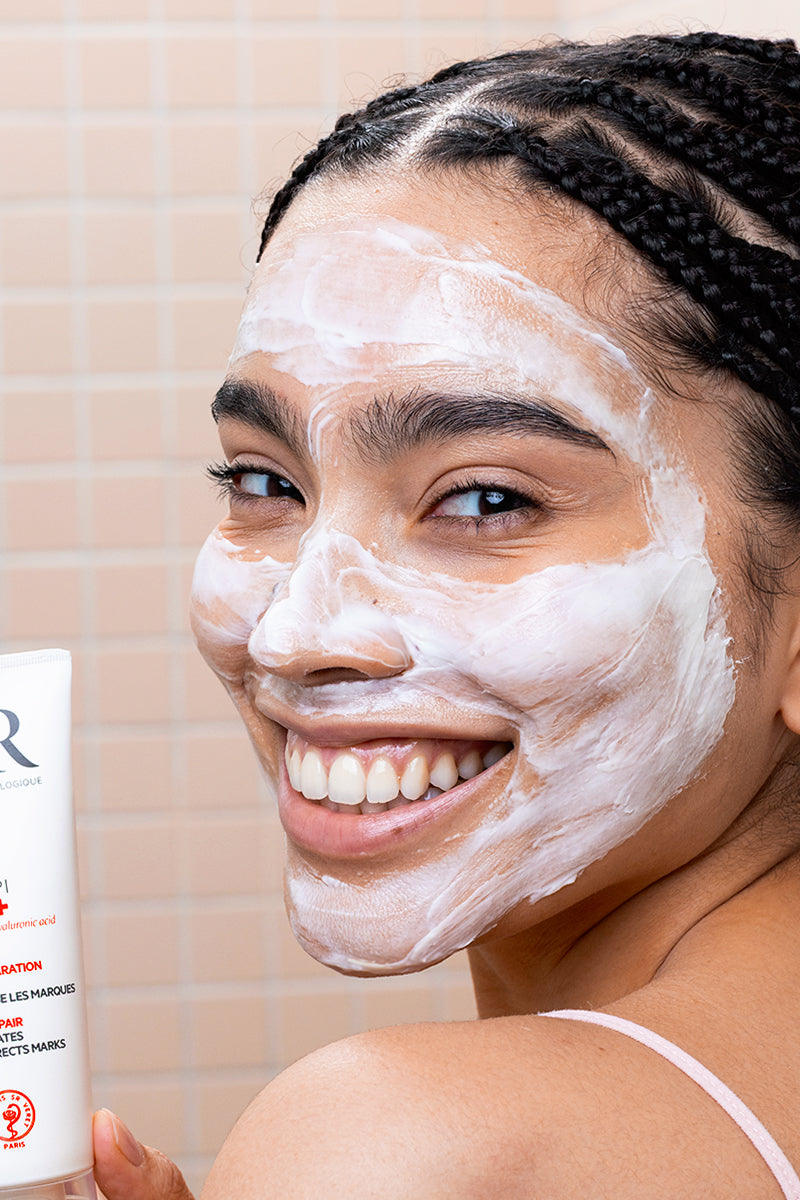 Smiling woman with white CICAVIT+ HPPI Crème on her face holding the white SVR skincare tube.