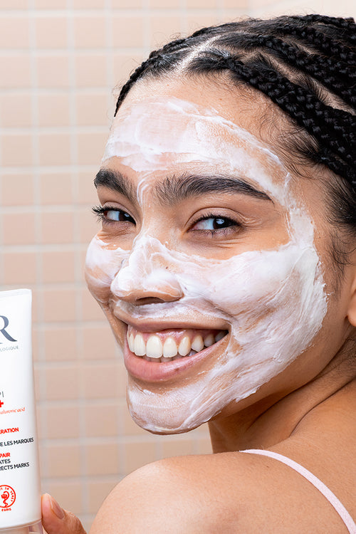 Smiling woman with white CICAVIT+ HPPI Crème on her face holding the white SVR skincare tube.