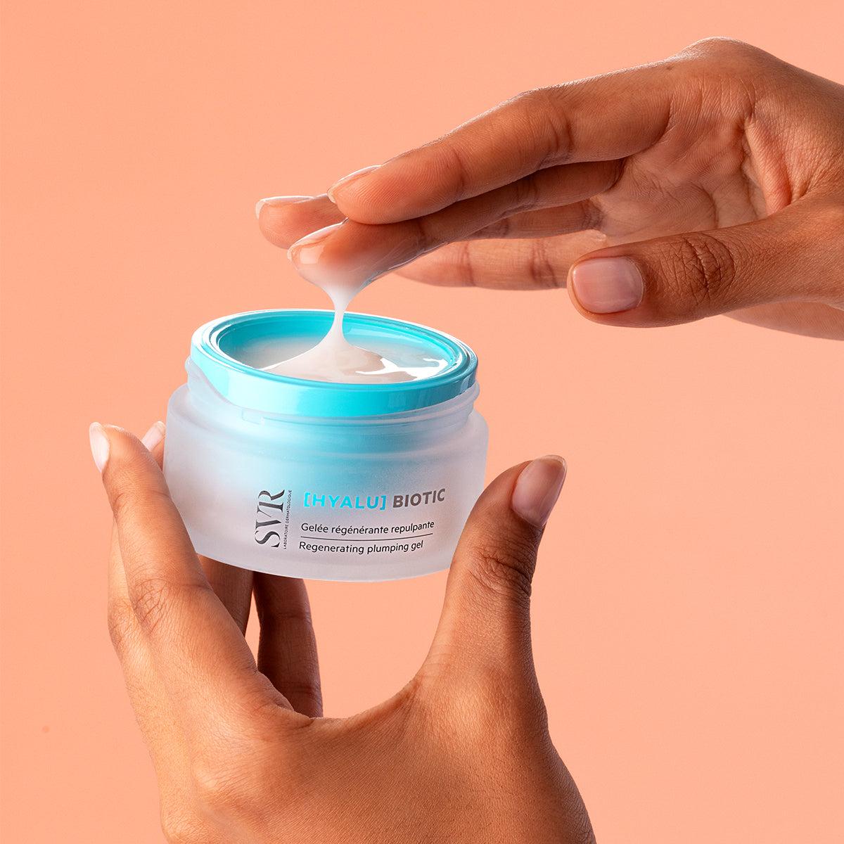 Hands holding a frosted glass jar of SVR Hyalu Biotic plumping gel with a bright blue lid and a creamy white texture.