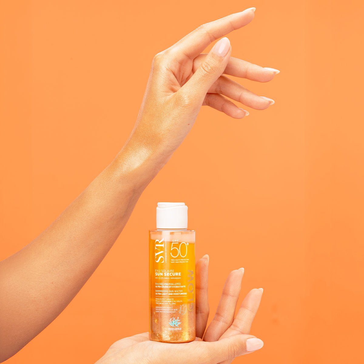 SVR SUN SECURE Eau Solaire GLOW SPF50+ bottle held by hand against an orange background with shimmering skin application.