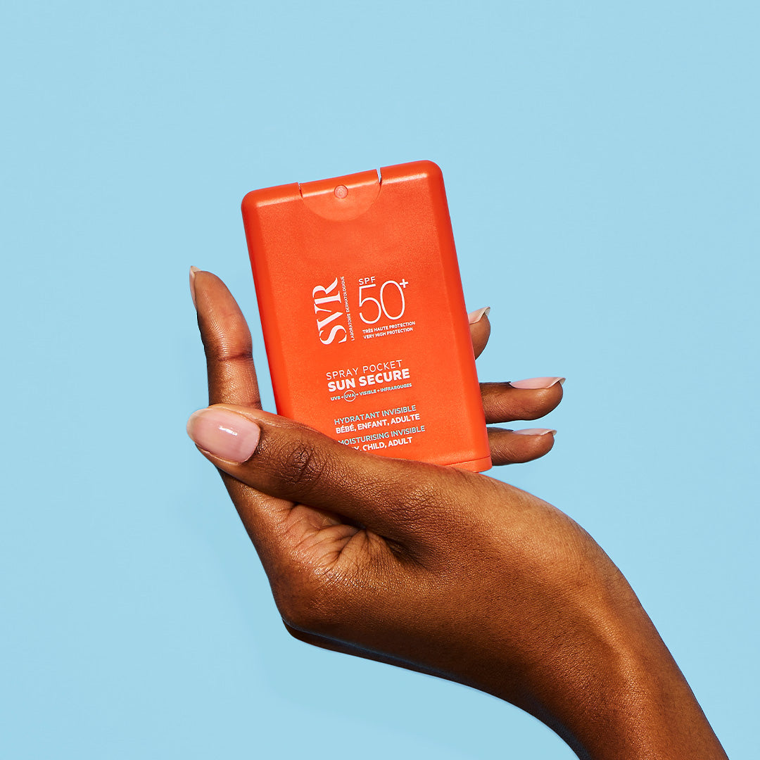Hand holding a compact, bright orange SVR SUN SECURE SPF50+ spray bottle against a light blue background.